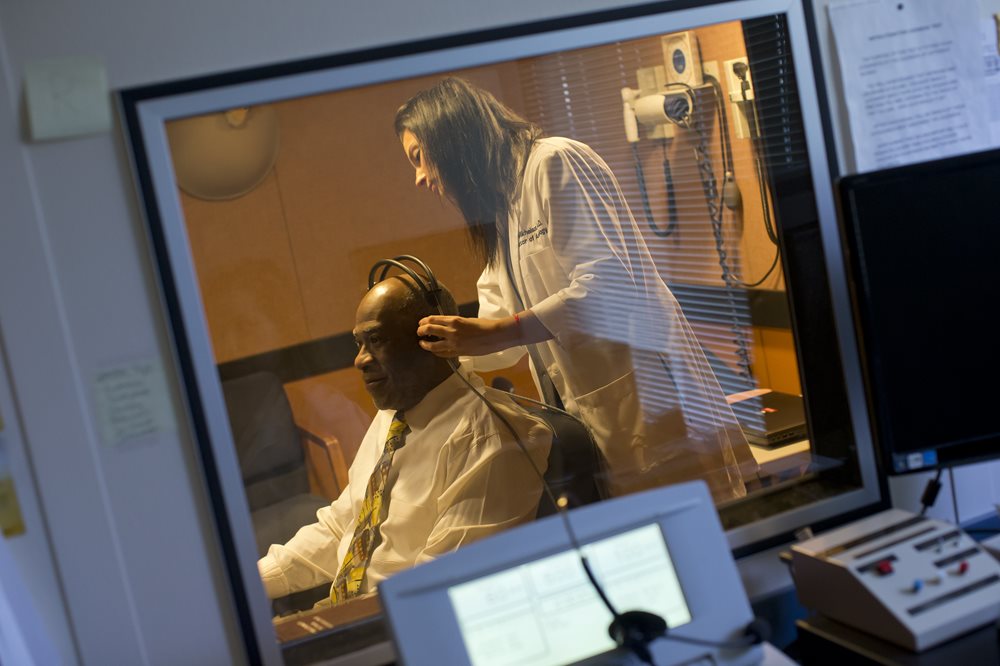 Audiologist places over the ear headphones onto elderly patient for a hearing test