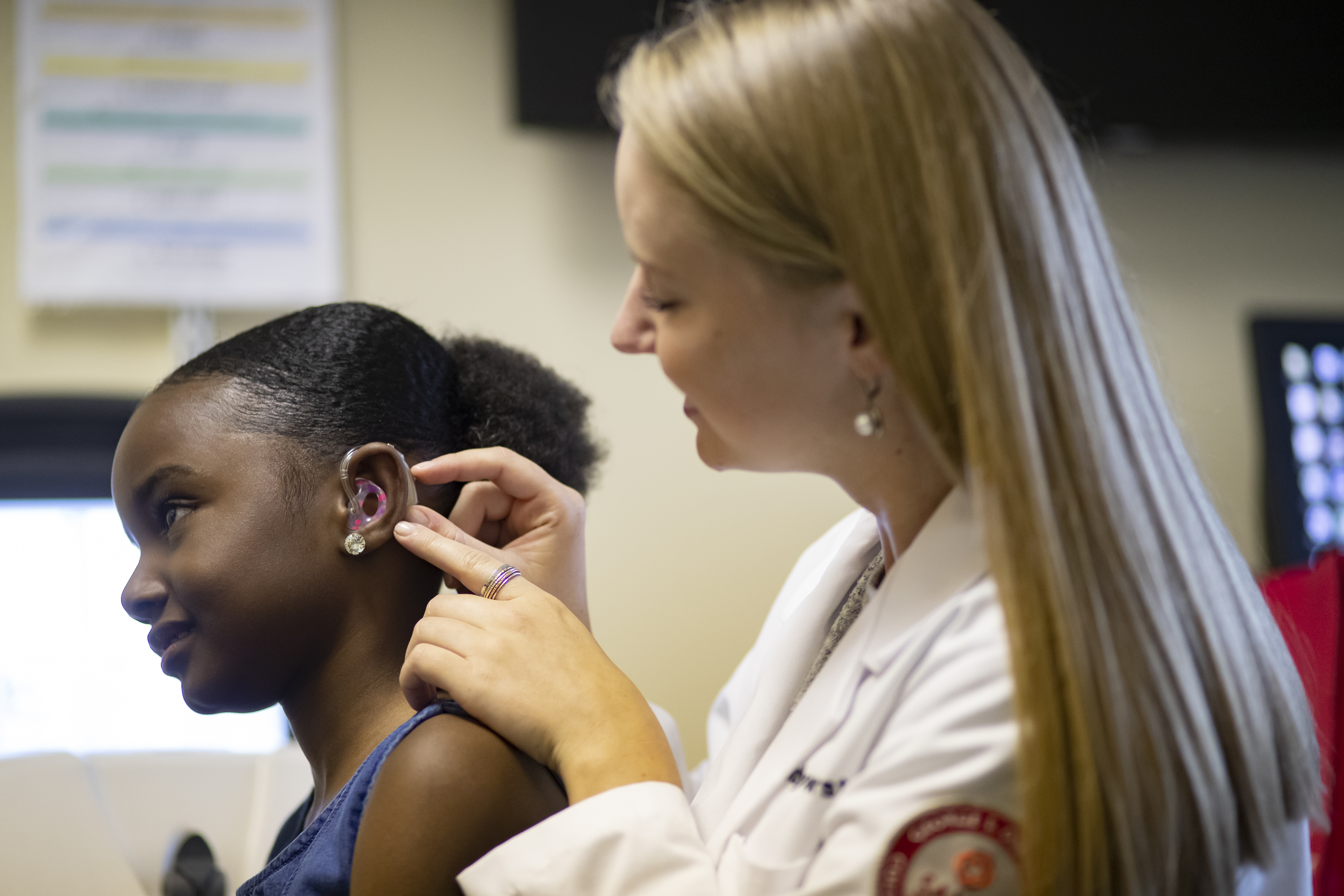 Audiologist fitting hearing aid onto child patient