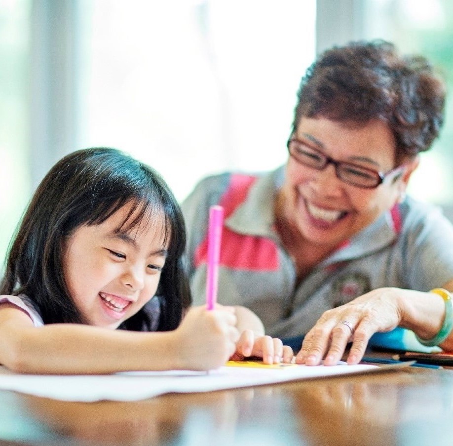 Young girl writing with mom looking on