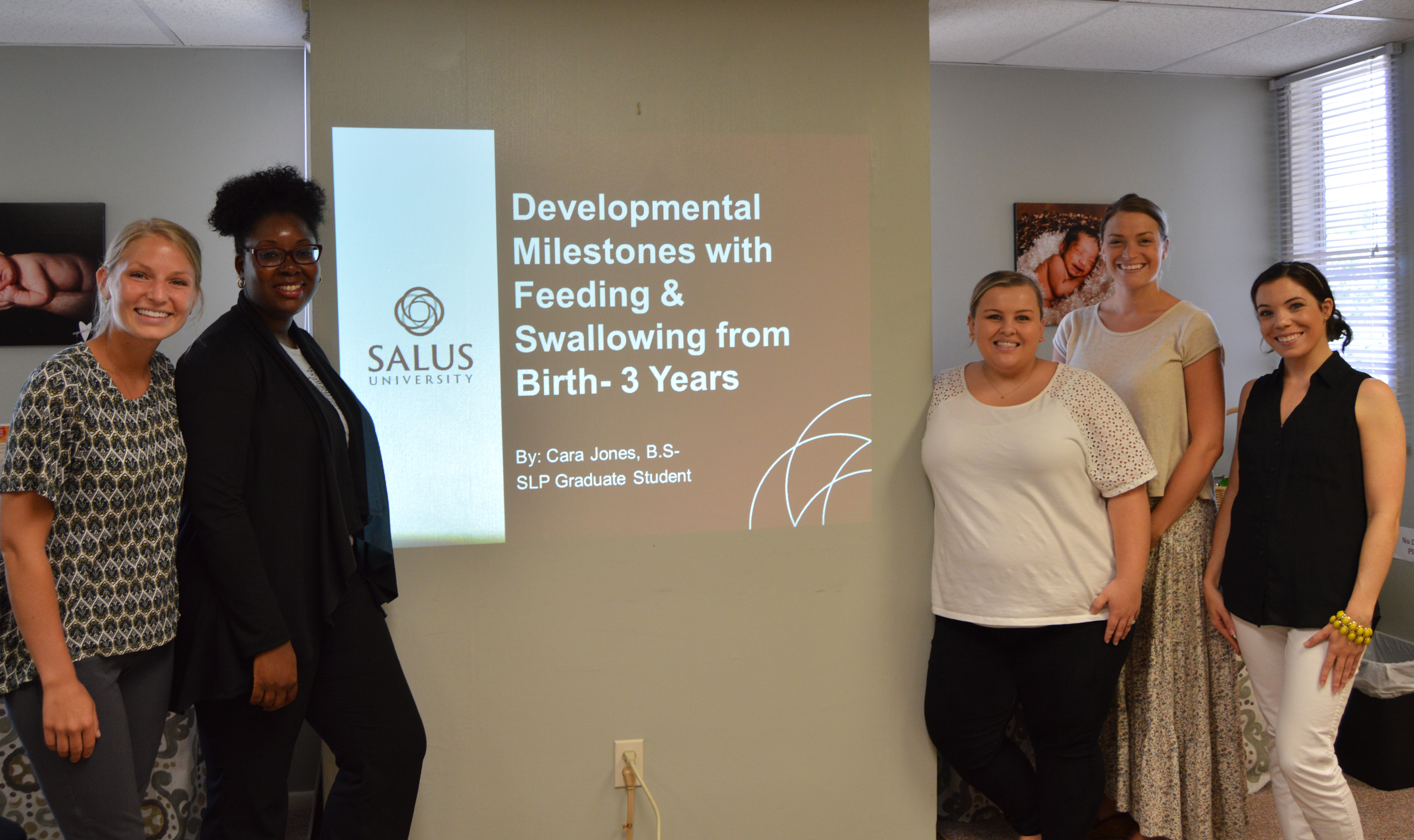 Students in front of a "developmental milestones with feeding and swallowing from birth - 3 years" presentation