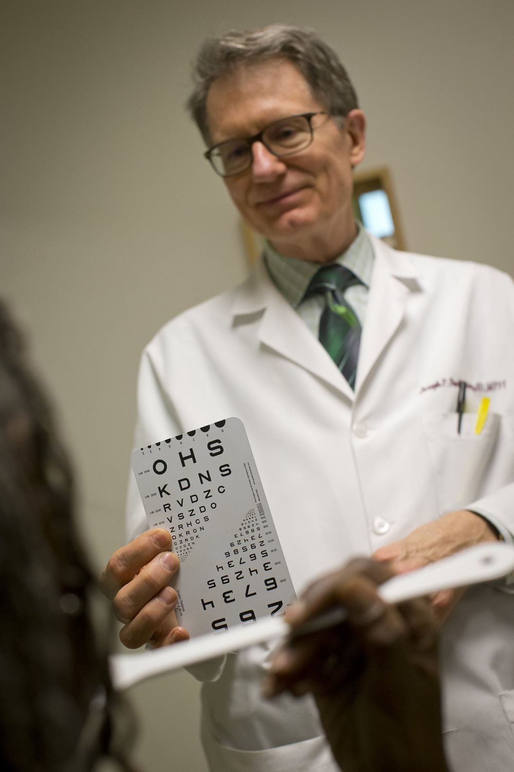 Doctor holding an eye chart in front of a patient