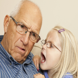 Child talking into grandfather's ear