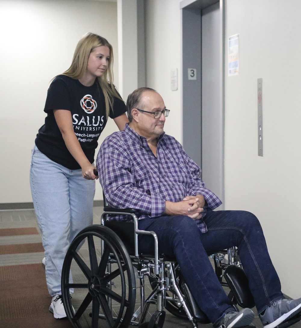 older man in wheelchair being pushed by a Salus OT student