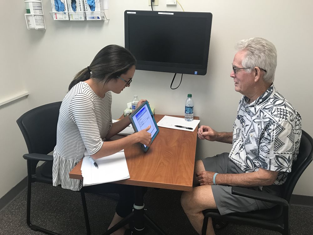 Speech-language pathologist holding a tablet sitting across a patient who has aphasia.