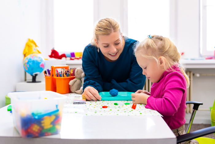 Toddler playing with clay, supervised by an adult